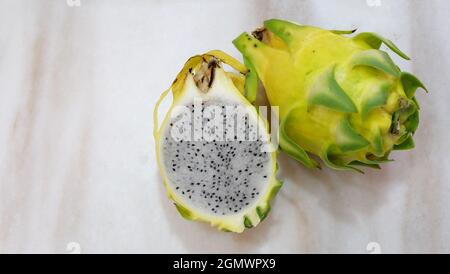 Eine ganze gelbe Drachenfrucht mit Haut und eine halbe Drachenfrucht daneben. Ansicht von oben, Kopierbereich links. Stockfoto