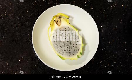 Flay einer weißen Platte in der Mitte platziert, mit einem halben Schnitt gelben Drachenfrucht darauf. Stockfoto