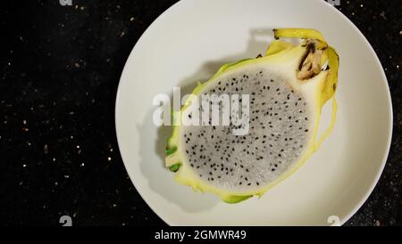 Nahaufnahme einer halben gelben Drachenfrucht, mit sichtbarem Fleisch, serviert auf einem weißen Teller. Ansicht von oben, mit Kopierplatz auf der linken Seite. Stockfoto