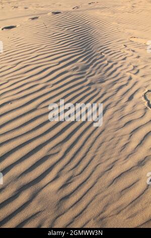 Fußabdrücke auf trockenem welligen Sandhintergrund an einem warmen Sommertag an der Ostsee am Liepaja-Strand, Lettland Stockfoto