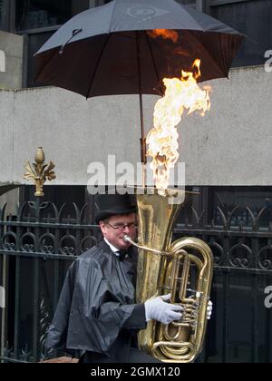London, England - 16. Oktober 2013 ein Mann bläst Tuba. Romanischer Straßenmusiker, der im Regen Musik spielt. Also braucht er wirklich diesen Regenschirm. Aber warum nicht Stockfoto