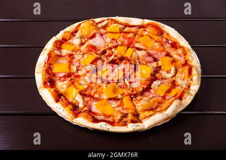 Eine ganze rustikale Pizza mit gebratenem Huhn, Speck und Teriyaki-Sauce wird auf einem Pappteller auf einem Holztisch serviert Stockfoto