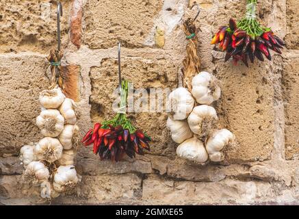 Ein Haufen scharfer Chilischoten und frischer weißer Knoblauch hängen an einer Steinmauer in einem Straßenmarkt Stockfoto