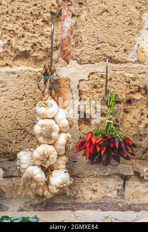 Ein Haufen scharfer Chilischoten und frischer weißer Knoblauch hängen an einer Steinmauer in einem Straßenmarkt, vertikal Stockfoto