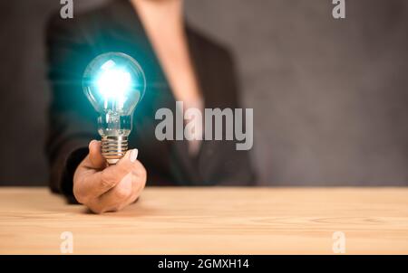 Idee Konzept. Geschäftsfrau hält eine leuchtend blaue Glühbirne. Frau gab eine innovative Idee. Nahaufnahme einer Frau, die einen glühenden Lig hält und zeigt Stockfoto