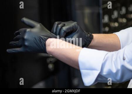 Koch trägt Plastikhandschuhe. Nahaufnahme der Hände mit schwarzen Latexschutzhandschuhen. Kein Gesicht Stockfoto