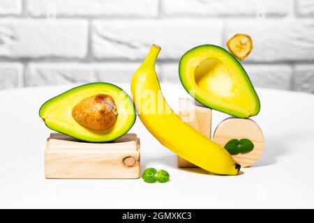 Kreative Avocado, Banane und Micro Green Balance Holzständer und Podien., weißer Hintergrund, Gleichgewicht gesunde Ernährung. Ausgewogenes Ernährungskonzept. Stockfoto