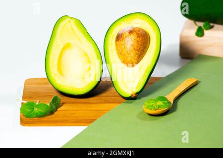 Hälften von reifen Avocado und Micro Green auf Holzbrett serviert auf dem Tisch, weißer Hintergrund, gesunde ölige Lebensmittel, Keto-Diät, Nahaufnahme. Stockfoto