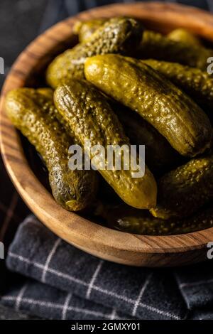 Kleine Gurken. Marinierte eingelegte Gurken in Holzschüssel auf schwarzem Tisch. Stockfoto