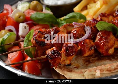 Gebratene Souvlaki, griechischer Salat und Tsatziki auf Holztisch. Hähnchenspieße Souvlaki, Pita-Brot - köstliches griechisches Mittagessen auf dunklem Hintergrund Stockfoto