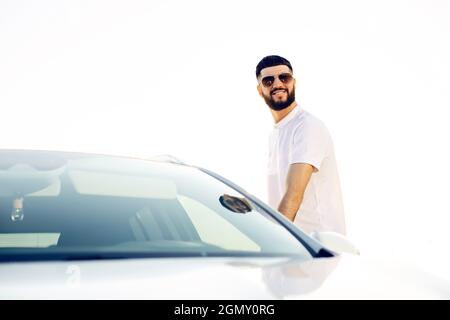 Selbstbewusster junger Geschäftsmann mit Sonnenbrille, Mann öffnet die Tür seines Autos, Mann sitzt in seinem Auto im Freien in der Stadt Stockfoto