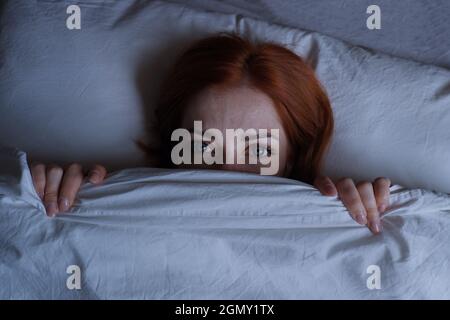 Schlaflose Frau, die nachts im Bett liegt und sich unter der Decke versteckt Stockfoto