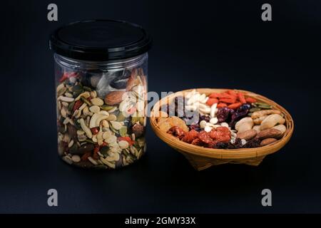 Vollkornprodukte und getrocknete Früchte in einer Bambusplatte und Plastikflasche auf schwarzem Hintergrund. Stockfoto