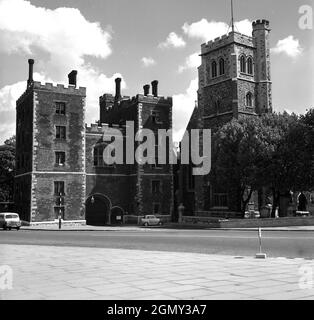 1950er Jahre, historisches Bild aus dieser Zeit des Lambeth Palace, London, England, Großbritannien, der offiziellen Londoner Residenz des Erzbischofs von Canterbury, von der Lambeth Road aus gesehen. Ursprünglich als Lambeth-Haus bekannt, wurde das Gebäude um 1200 n. Chr. von der Diözese erworben. Hier sieht man das von Kardinal John Morton erbaute Tudor-Backsteinhaus, das mit schwarzem Ruß bedeckt ist. Stockfoto