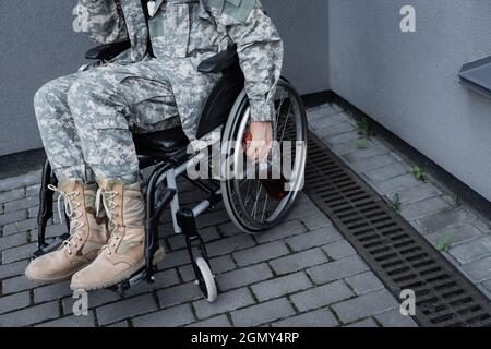Beschnittene Ansicht eines behinderten Soldaten, der im Rollstuhl sitzt und eine Flasche Whiskey im Freien hält Stockfoto