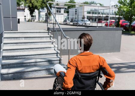 Rückansicht eines jungen behinderten Mannes im Rollstuhl in der Nähe einer Treppe auf der Straße Stockfoto