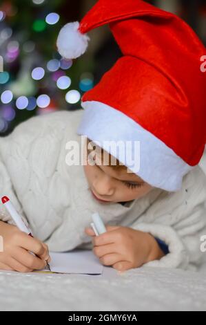 Ein Junge mit einem Neujahrshut schreibt einen Brief an den Weihnachtsmann Stockfoto