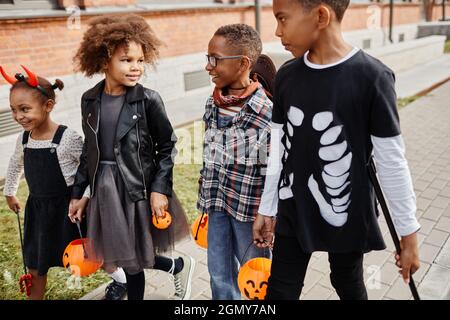 Eine Gruppe aufgeregter afroamerikanischer Kinder, die im Freien Halloween-Kostüme tragen, während sie sich mit anderen verwöhnen lassen Stockfoto