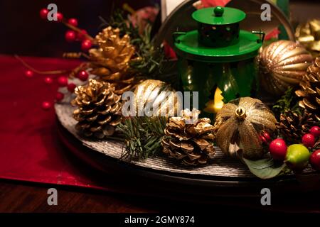 Nahaufnahme eines schwach beleuchteten Weihnachtsdisplays im Mittelpunkt, bestehend aus goldenen Glühbirnen, Kiefernzacken und einer Laterne. Stockfoto