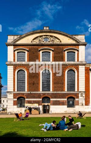 Junge Menschen, die in den Gärten des Old Royal Navy College, Greenwich, London, Großbritannien, sitzen. Stockfoto