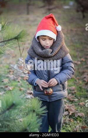 Ein Junge in einem Neujahrshut schmückt einen Weihnachtsbaum im Freien Stockfoto