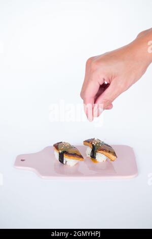 Japanisches Sushi: Zwei Unagi Nigiri-Sushi auf hellrosa Tafel. Aal-Sushi. Nahaufnahme des Zubereitungsvorgangs von Sushi. Isoliert auf Weiß Stockfoto