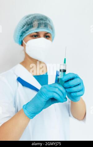 Eine Ärztin mit einer medizinischen Gesichtsmaske und Handschuhen wählt den Impfstoff aus einer Ampulle in eine Spritze. Nahaufnahme des Arztes. Impfung gegen Infektionskrankheiten und Erkältungen. Stockfoto
