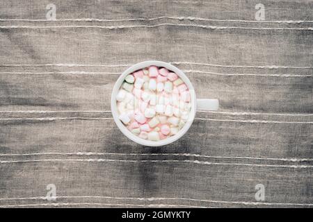 Tasse Kakao mit Sumpflaibe auf grauem Textilhintergrund. Draufsicht, flach liegend. Stockfoto