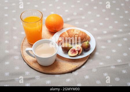 Croissant auf einem Teller mit Feigen, einer Kaffeetasse, Orangensaft und einer Orange auf einem Tablett. Traditionelles Frühstückskonzept. Stockfoto