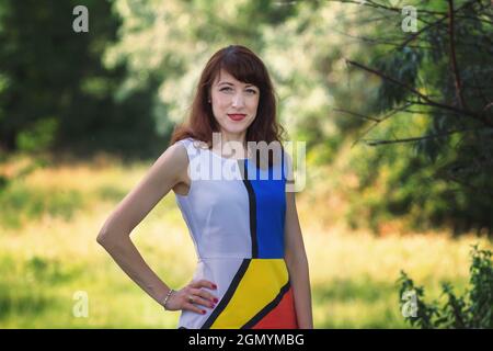 Schöne lächelnde junge Brünette Frau trägt bunte Kleid posiert in einem Park. Stockfoto