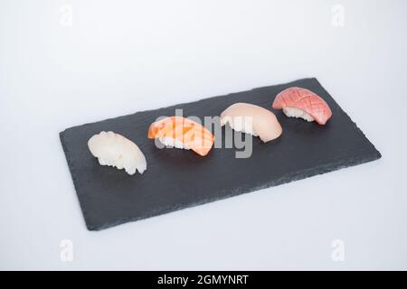 Vier Sushi-Nigiri auf dem schwarzen Schiefer auf weißem Hintergrund. Traditionelles japanisches Essen. Ansicht von oben. Hochwertige Fotos Stockfoto