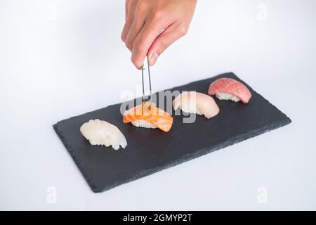 Sushi Nigiri auf schwarzem Tablett serviert. Vier Sushi-Stücke auf schwarzem Schiefer auf weißem Hintergrund isoliert serviert. Japanisches Essen. Der Küchenchef schmückt Sushi Stockfoto