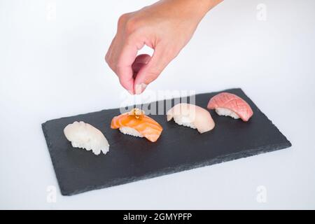 Sushi Nigiri auf schwarzem Tablett serviert. Vier Sushi-Stücke auf schwarzem Schiefer auf weißem Hintergrund serviert. Traditionelles japanisches Essen. Der Küchenchef schmückt Sushi Stockfoto