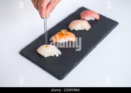 Sushi Nigiri auf schwarzem Tablett serviert. Vier Sushi-Stücke auf schwarzem Schiefer auf weißem Hintergrund isoliert serviert. Japanisches Essen. Der Küchenchef schmückt Sushi Stockfoto