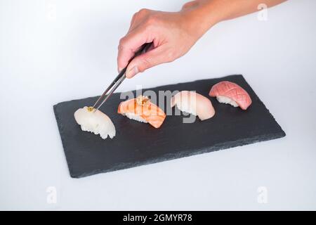 Sushi Nigiri auf schwarzem Tablett serviert. Vier Sushi-Stücke auf schwarzem Schiefer auf weißem Hintergrund isoliert serviert. Japanisches Essen. Der Küchenchef schmückt Sushi Stockfoto