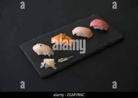 Sushi-Set auf schwarzem Tablett. Vier verschiedene Sushi-Stücke auf schwarzem Schiefer mit Ingwer. Traditionelles japanisches Essen auf schwarzem Hintergrund. Stockfoto