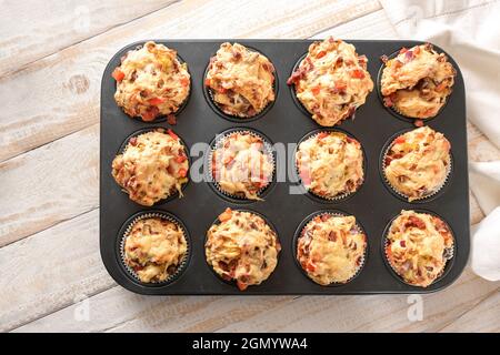 Backblech mit hausgemachten Pizza-Muffins aus Hefeteig, Tomaten, Gemüse, Wurst und Käse frisch aus dem Ofen auf einem Holztisch, Hochwinkel V Stockfoto