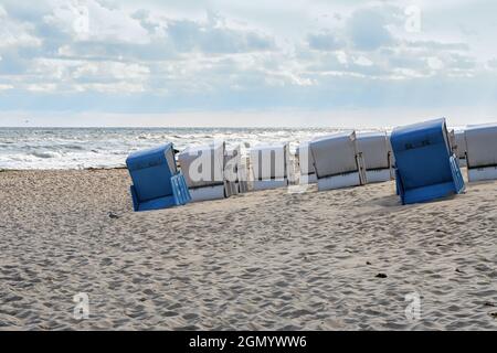 Liegestühle in blau und weiß von hinten, schräg auf dem Sand vor den Wellen am Ufer der Ostsee stehend, sonniger Himmel mit Wolken, c Stockfoto