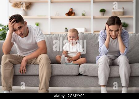 Familienkonflikte. Nettes Kleinkind Baby sitzt zwischen beleidigten Eltern nach Streit zu Hause, junge Ehegatten mit Kind leiden eheliche Krise, Gefühl Stockfoto