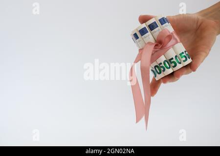 Weibliche Hand hält 50 Euro Scheine in Rollen, gebunden mit rosa Geschenkband. Stockfoto