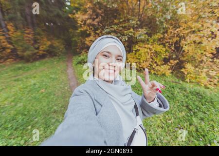 Modische junge muslimische asiatische Mädchen in Hijab nimmt ein Selfie auf dem Smartphone im Freien im Herbst Park Stockfoto