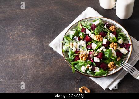 Rüben- oder Rote Beete-Salat mit frischer Rucola, Weichkäse und Walnüssen auf dem Teller, Dressing und Gewürzen auf dunklem Holzhintergrund, Kopierraum, Draufsicht/ Stockfoto