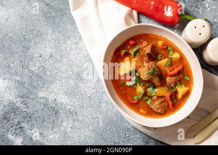 Gulasch ist ein traditionelles ungarisches Gericht mit Rindfleisch, Kartoffeln, Tomaten und Paprika. Gulasch in weißen Tellern mit Gemüse zum Kochen. Stockfoto