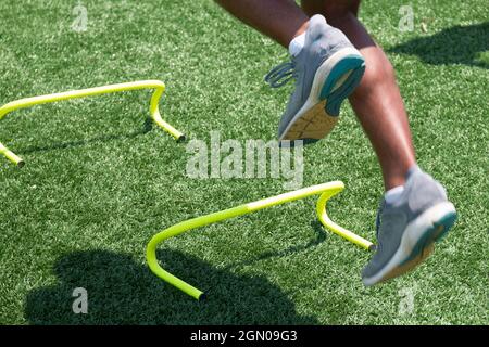 Männlicher Athlet, der über gelbe Mini-Hürden auf einem grünen Rasenfeld springt, in der Nähe mit Bewegungsunschärfen, die die Geschwindigkeit der dports-Übung zeigen. Stockfoto