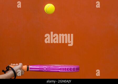 Hand hält Einen Paddle Tennis Racket und schlägt den Ball auf einem orangefarbenen Hintergrund.Sport Stockfoto
