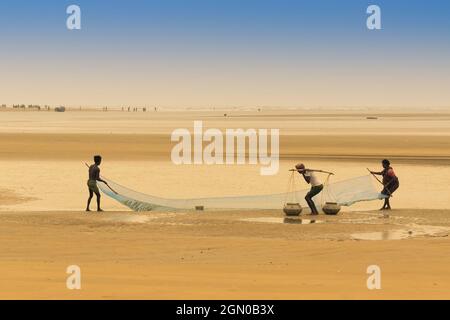 TAJPUR, WESTBENGALEN, INDIEN - 22. JUNI 2014 : Ein Fischer, der mit seiner Frau und seinem Sohn Fische mit Fischernetz am Ufer der Bucht von Bengalen fängt. Angeln Stockfoto