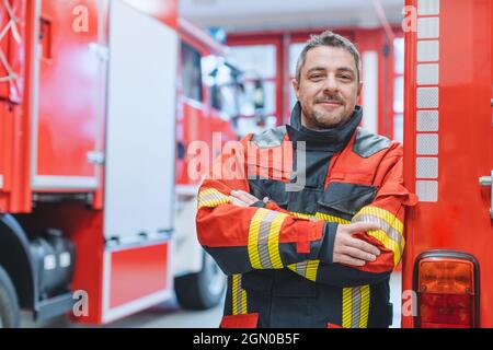 Erfahrener Feuerwehrmann, der vor einem Feuerwehrwagen steht Stockfoto