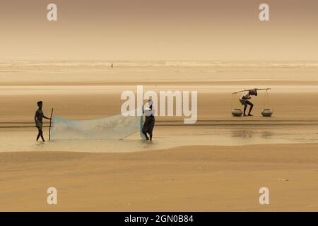 TAJPUR, WESTBENGALEN, INDIEN - 22. JUNI 2014 : Ein Fischer, der mit seiner Frau und seinem Sohn Fische mit Fischernetz am Ufer der Bucht von Bengalen fängt. Angeln Stockfoto