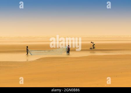 TAJPUR, WESTBENGALEN, INDIEN - 22. JUNI 2014 : Ein Fischer, der mit seiner Frau und seinem Sohn Fische mit Fischernetz am Ufer der Bucht von Bengalen fängt. Angeln Stockfoto