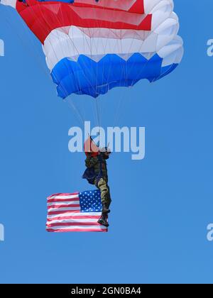 Fallschirmspringer steigt bei einer Flugschau unter einem rot-weiß-blauen Baldachin mit der Flagge der Vereinigten Staaten ab. Stockfoto